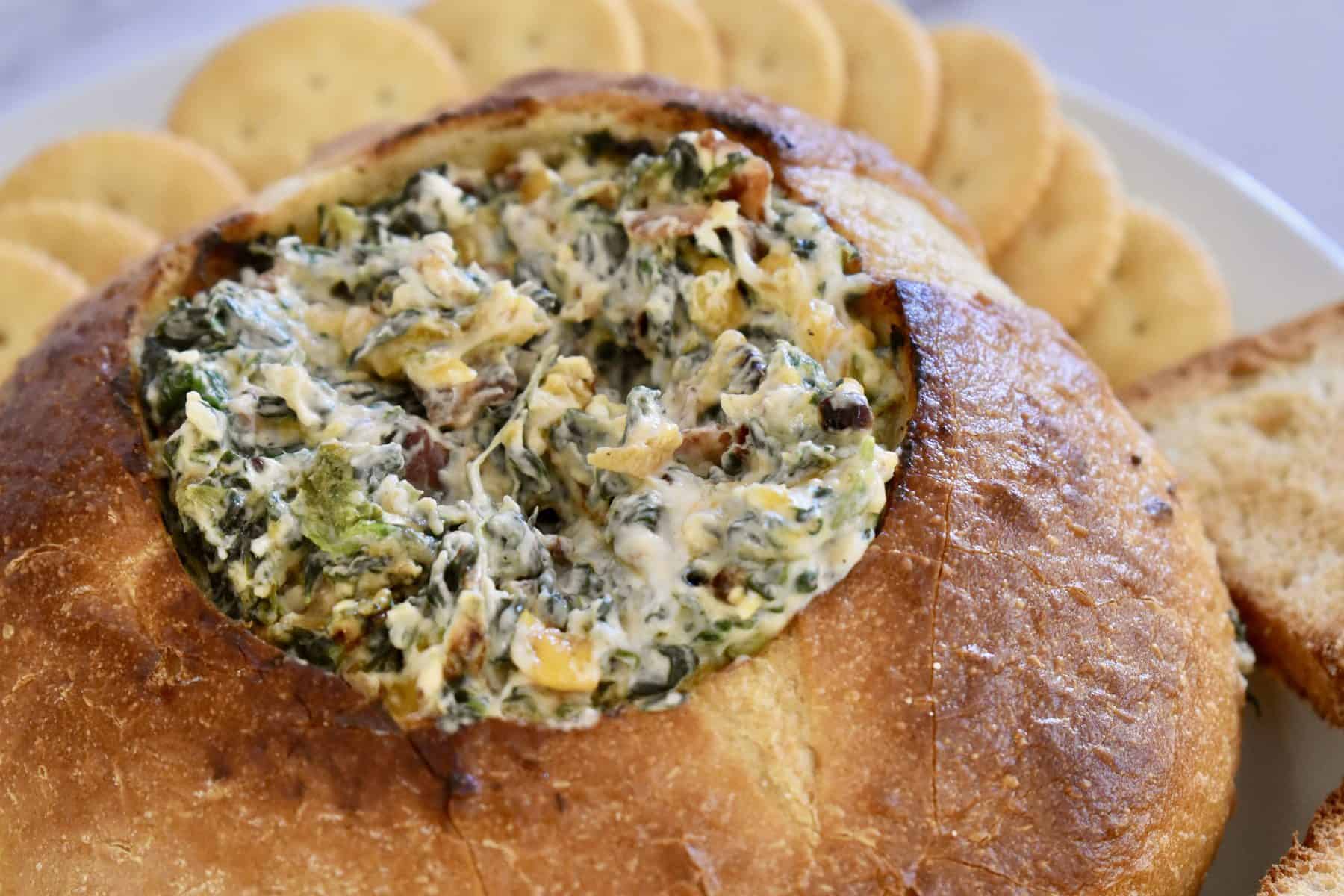 Close up view of hollowed out sourdough loaf with bacon spinach dip inside.