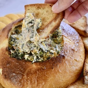 Bacon Spinach Dip Loaf with a piece of bread dipped in it.
