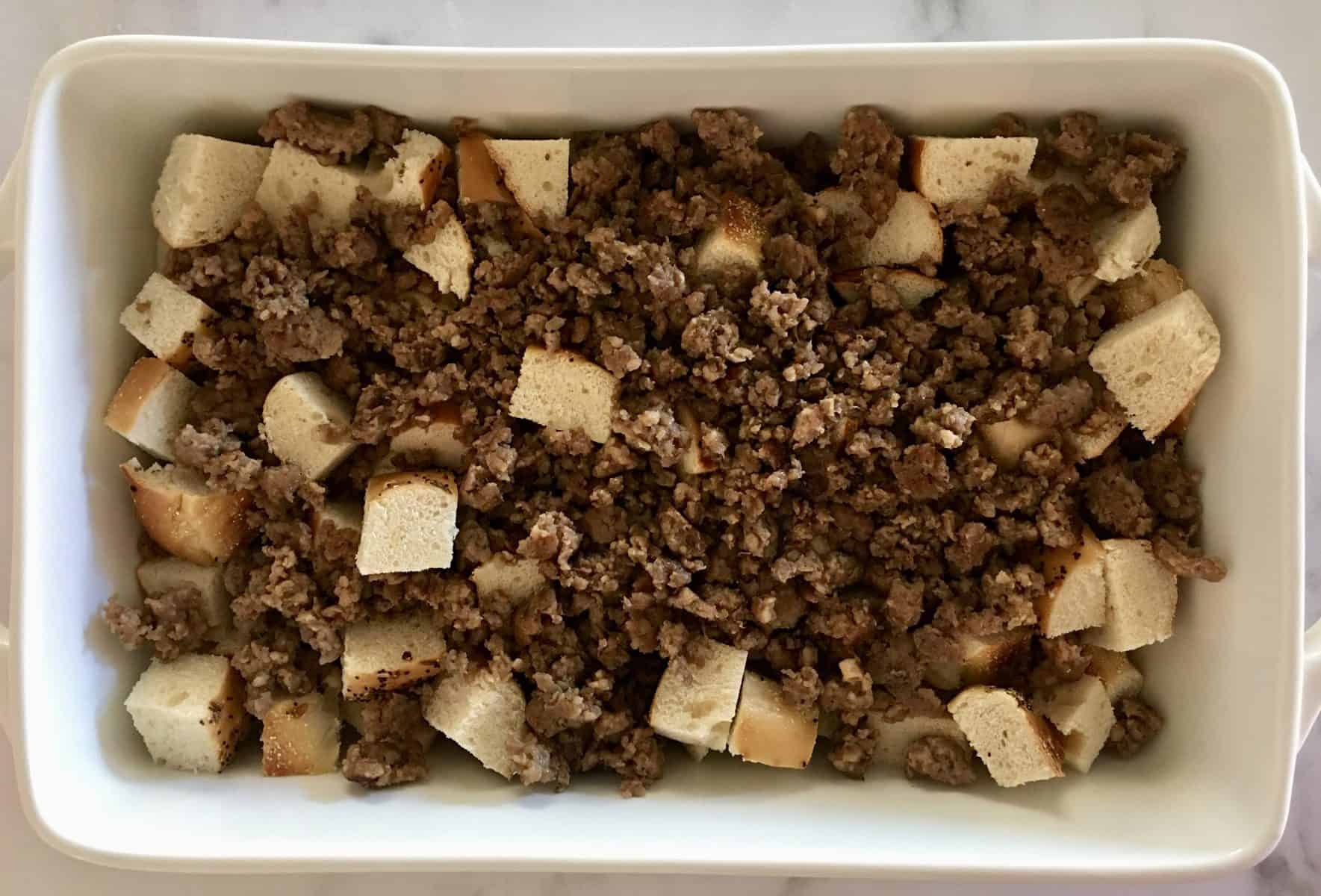 Cut up bread and cooked meat in a white casserole dish. 