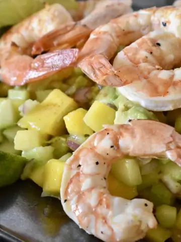 Shrimp mango cucumber salad on a plate with lime wedges.