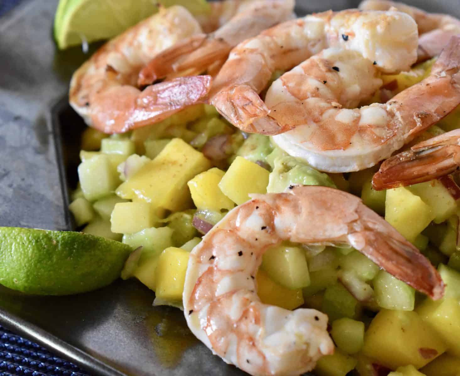 Shrimp mango cucumber salad on a plate with lime wedges.