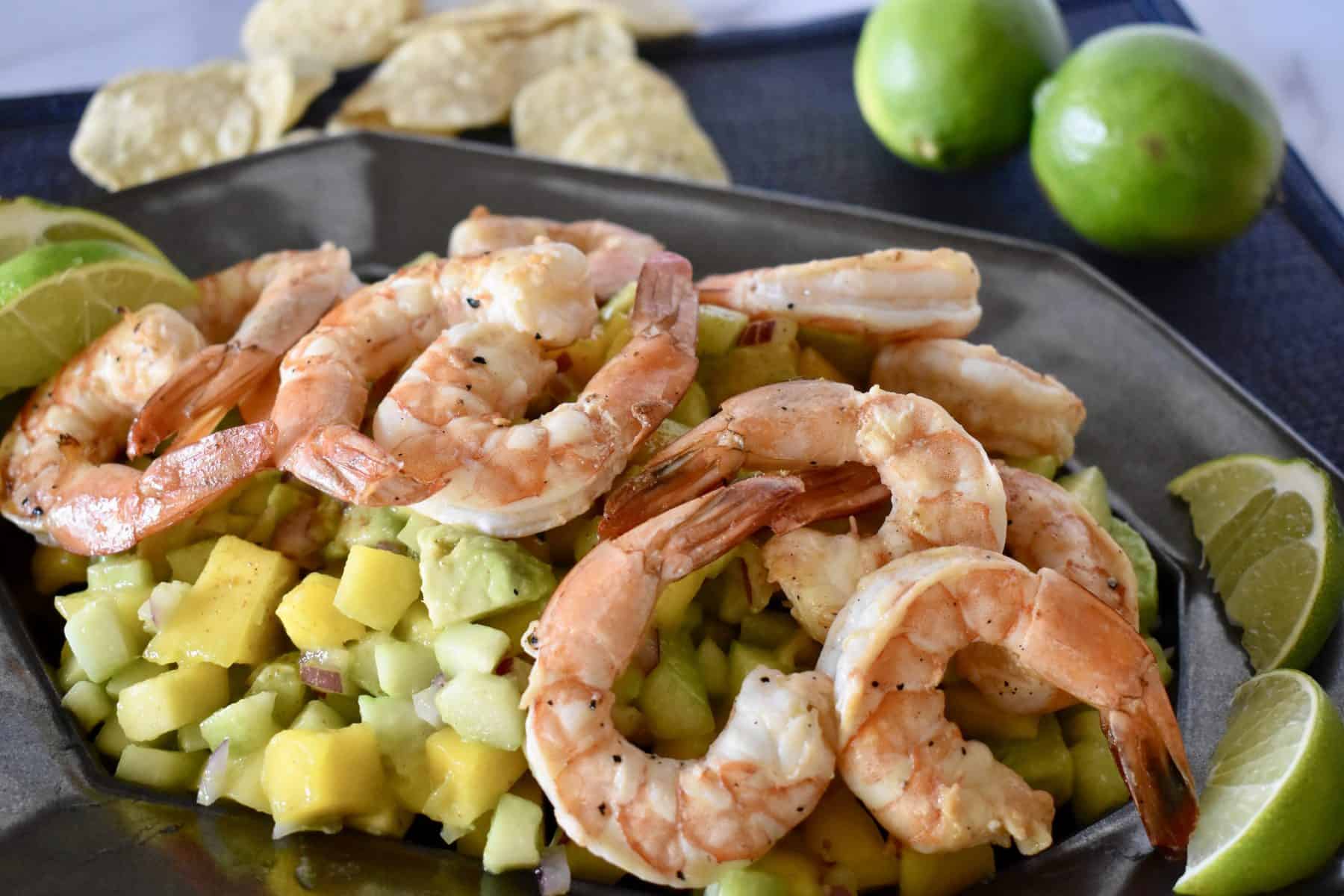 Shrimp on a bed of mango cucumber salad with tortilla chips it the background. 