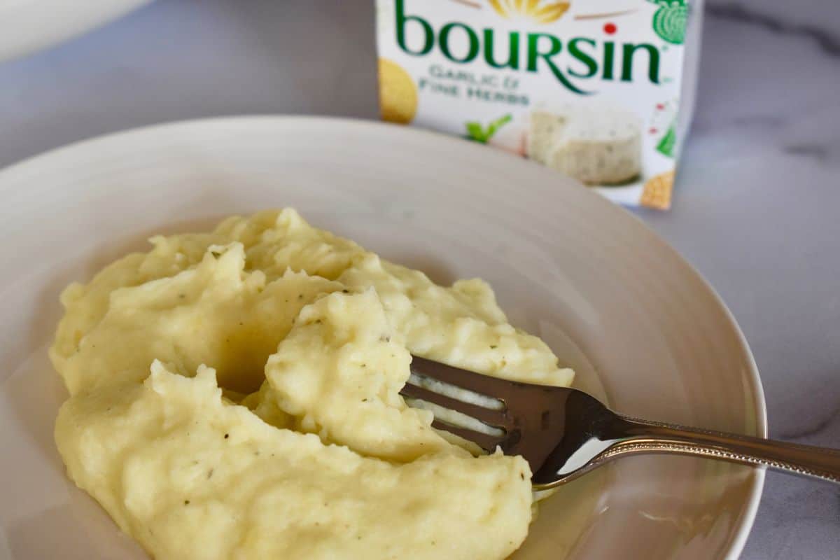 Boursin mashed potatoes on a plate with a fork and a box of boursin cheese in the background. 
