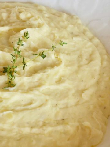 Boursin mashed potatoes in a white bowl with a sprig of thyme on top.