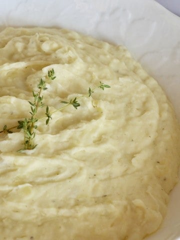 Boursin Mashed Potatoes with a garlic and herb Boursin cheese next to the white bowl.