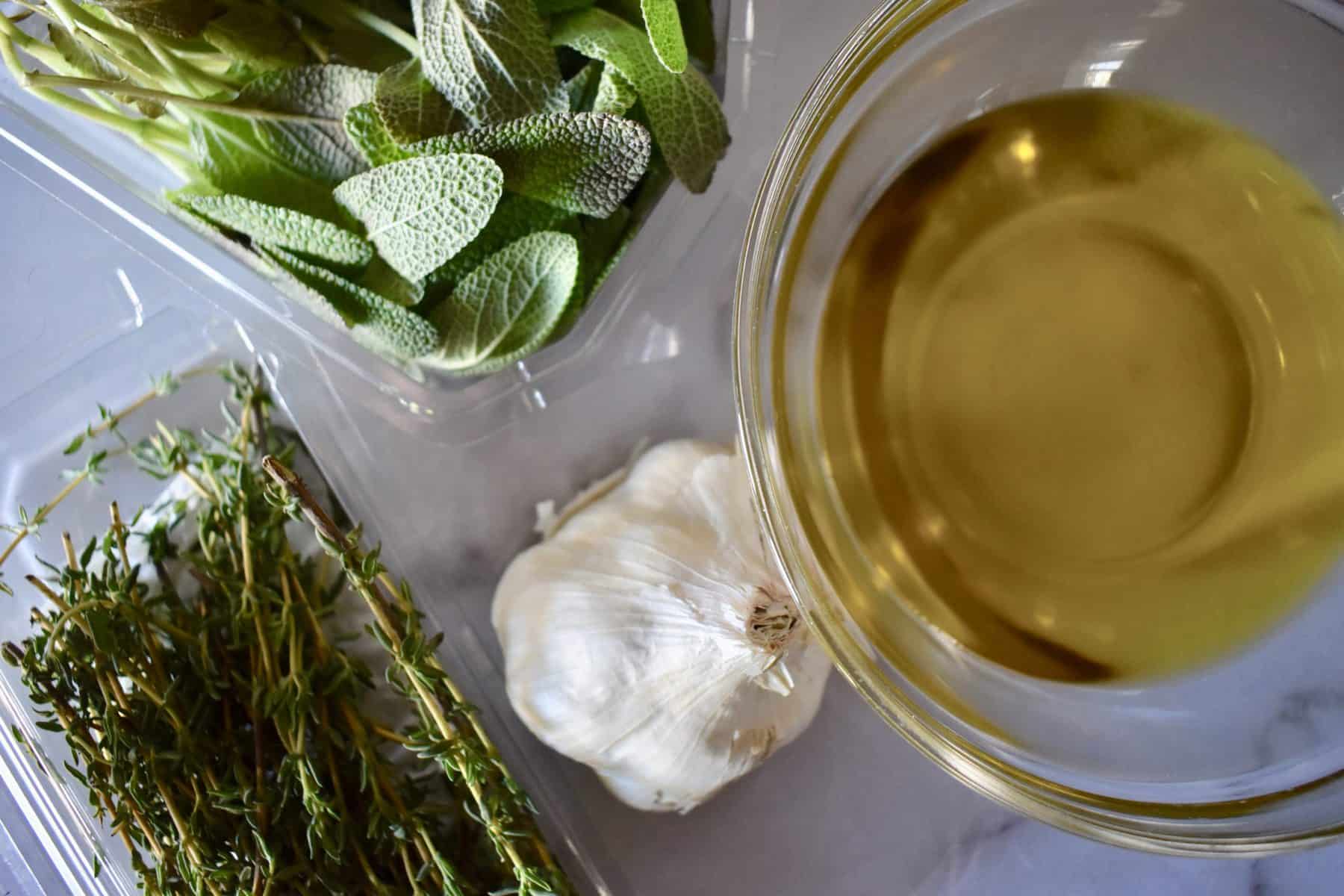 Garlic, thyme, sage, and olive oil on a countertop. 