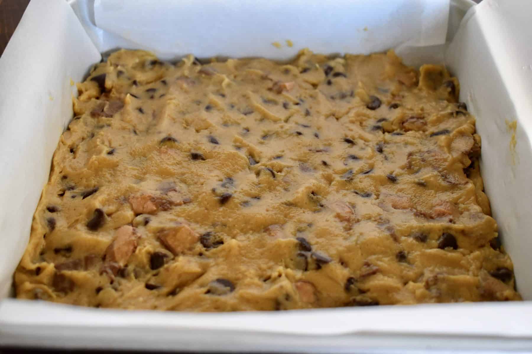 blondie batter pressed into the bottom of a parchment lined baking pan. 