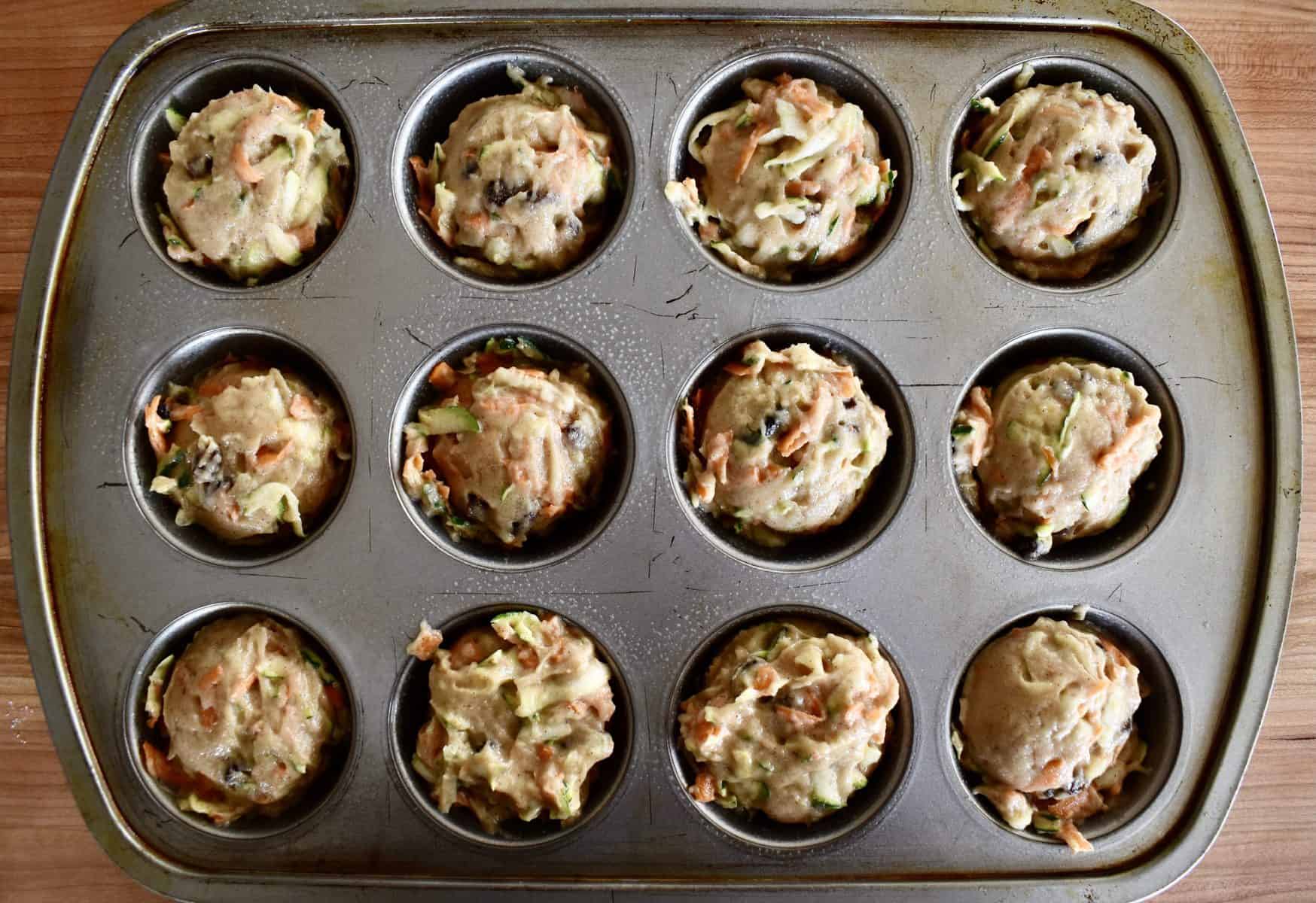 muffin tins filled with zucchini carrot raisin muffin batter. 