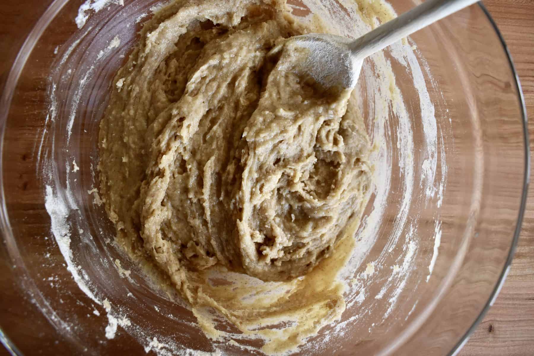 wet and dry ingredients mixed together in a glass bowl with a wooden spoon. 