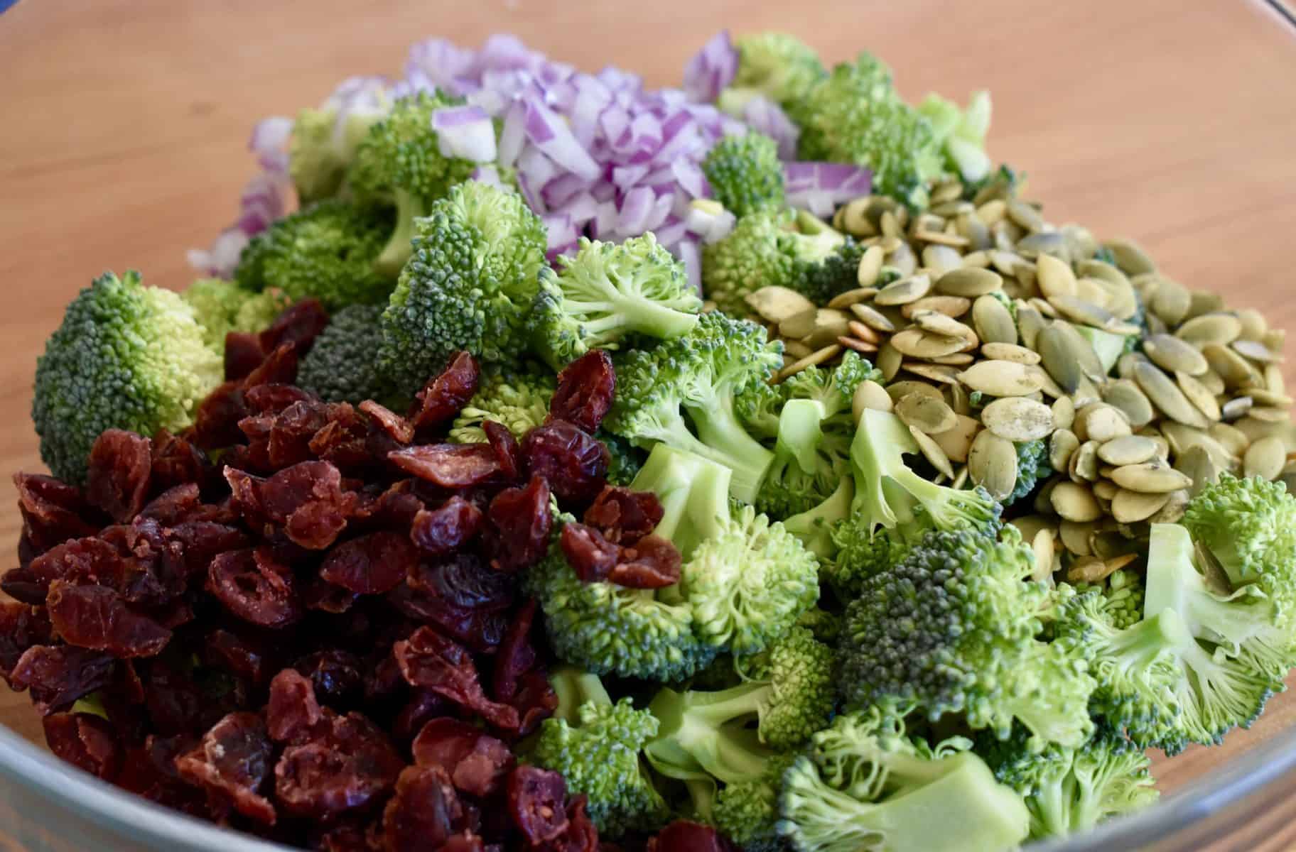 broccoli, cranberries, red onions, and sunflower seeds in a large glass bowl. 