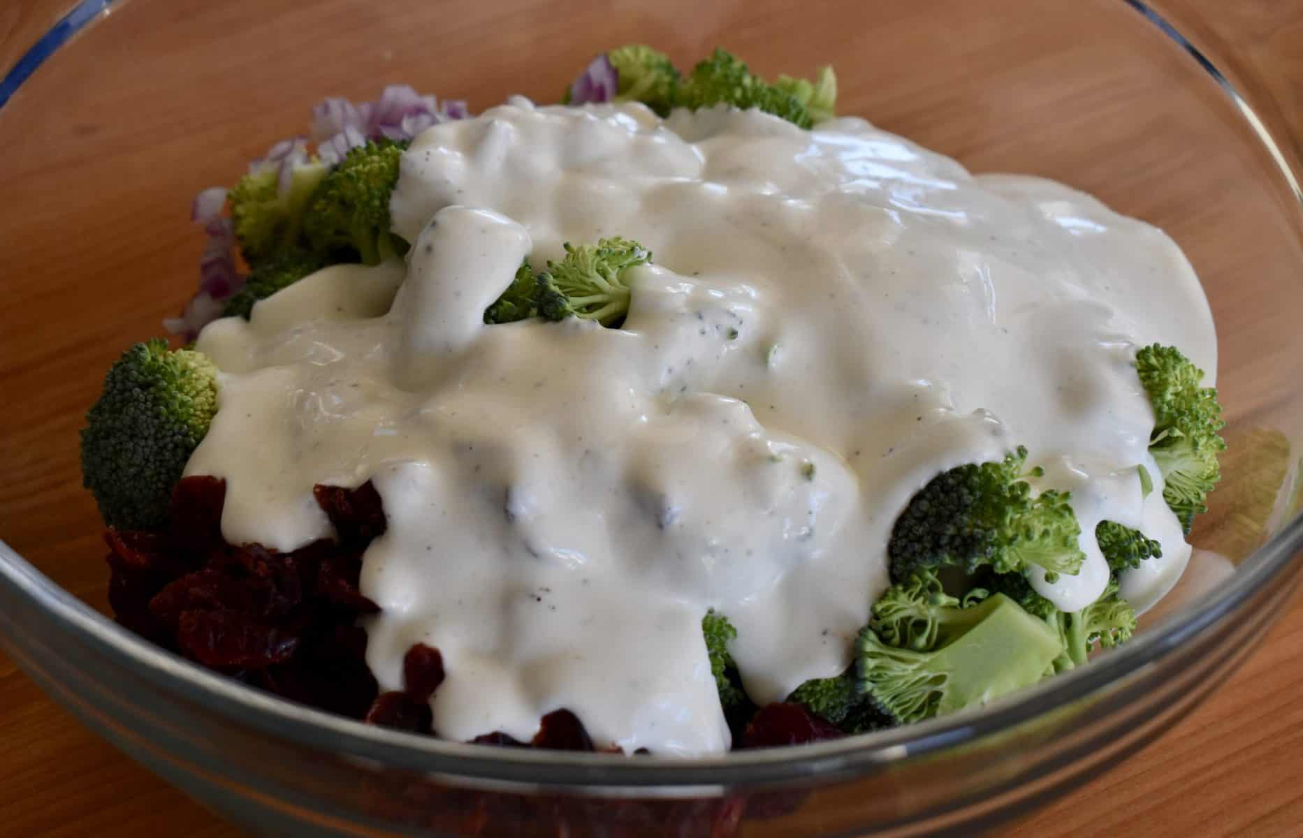 greek yogurt dressing poured over broccoli cranberry salad in a large glass bowl. 