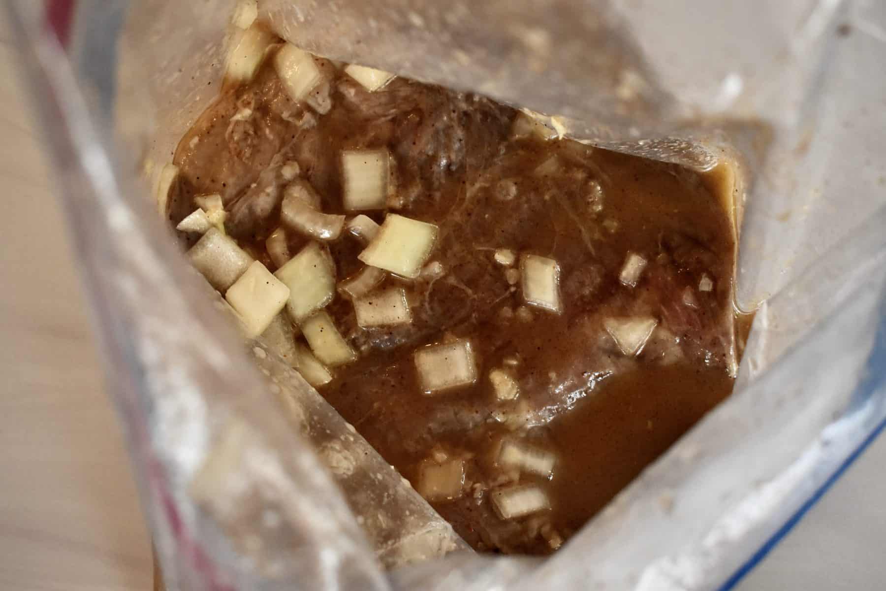Onions, lime, and other ingredients in a large plastic bag with flank steak inside. 