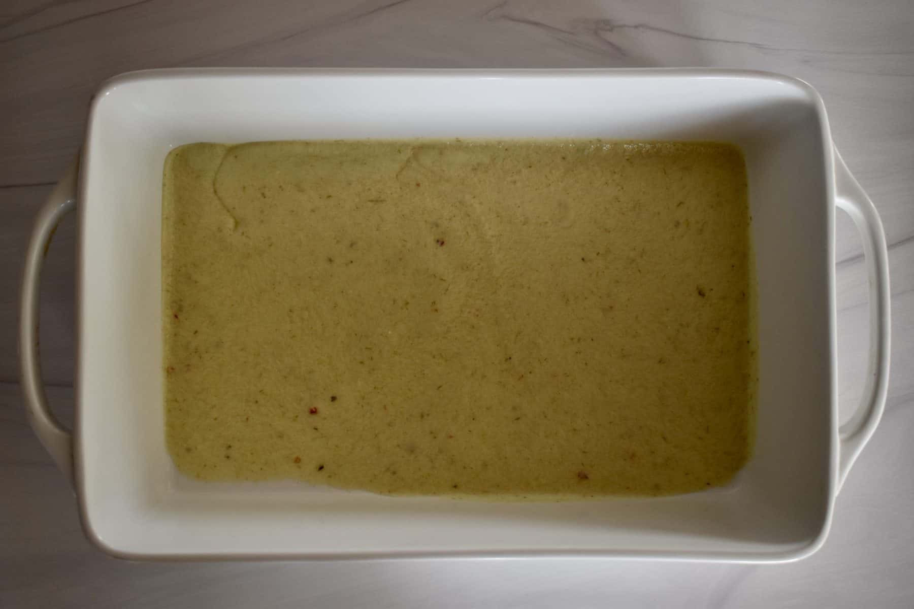 green enchilada sauce on the bottom of a white casserole dish. 