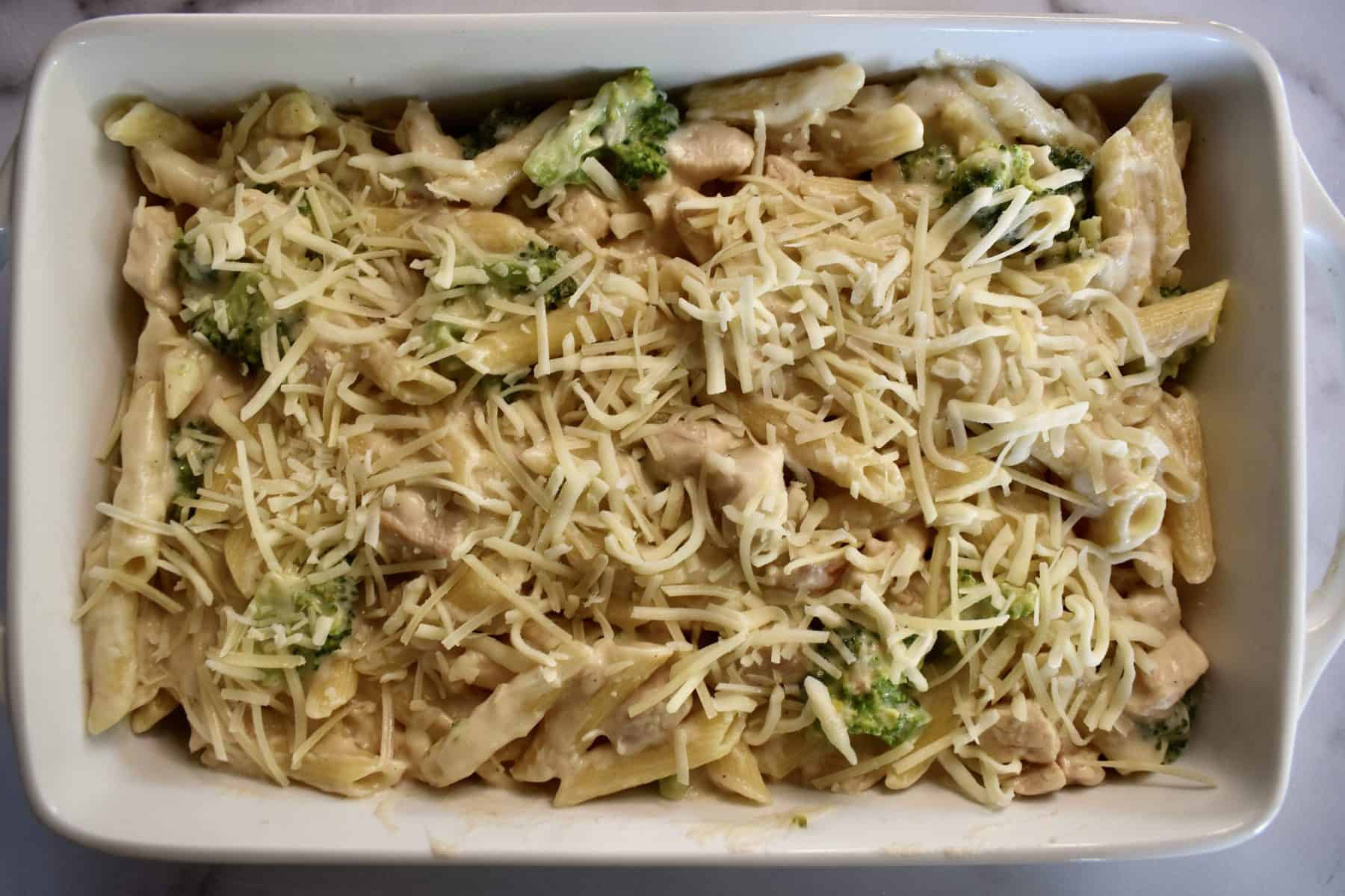 Pan of penne Alfredo with shredded cheese on top.