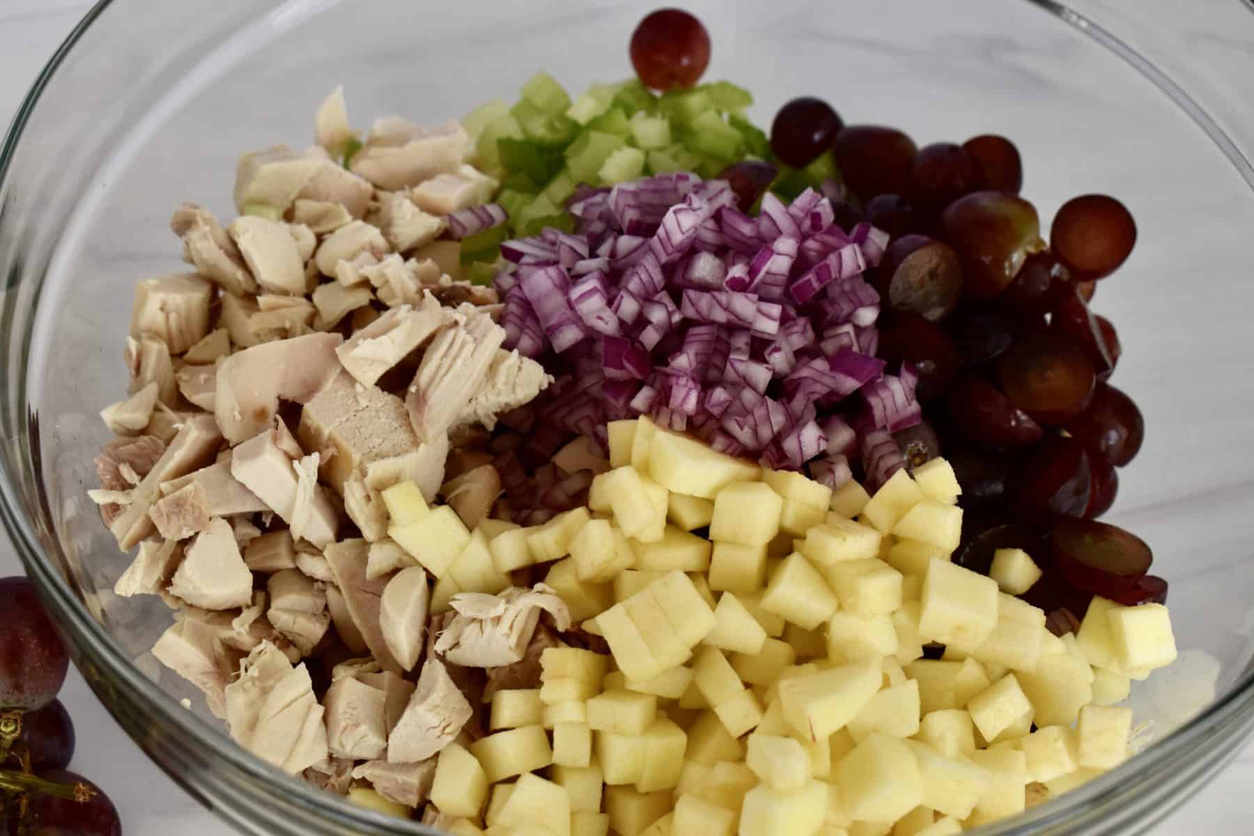 Ingredients for rotisserie chicken salad in a glass bowl.