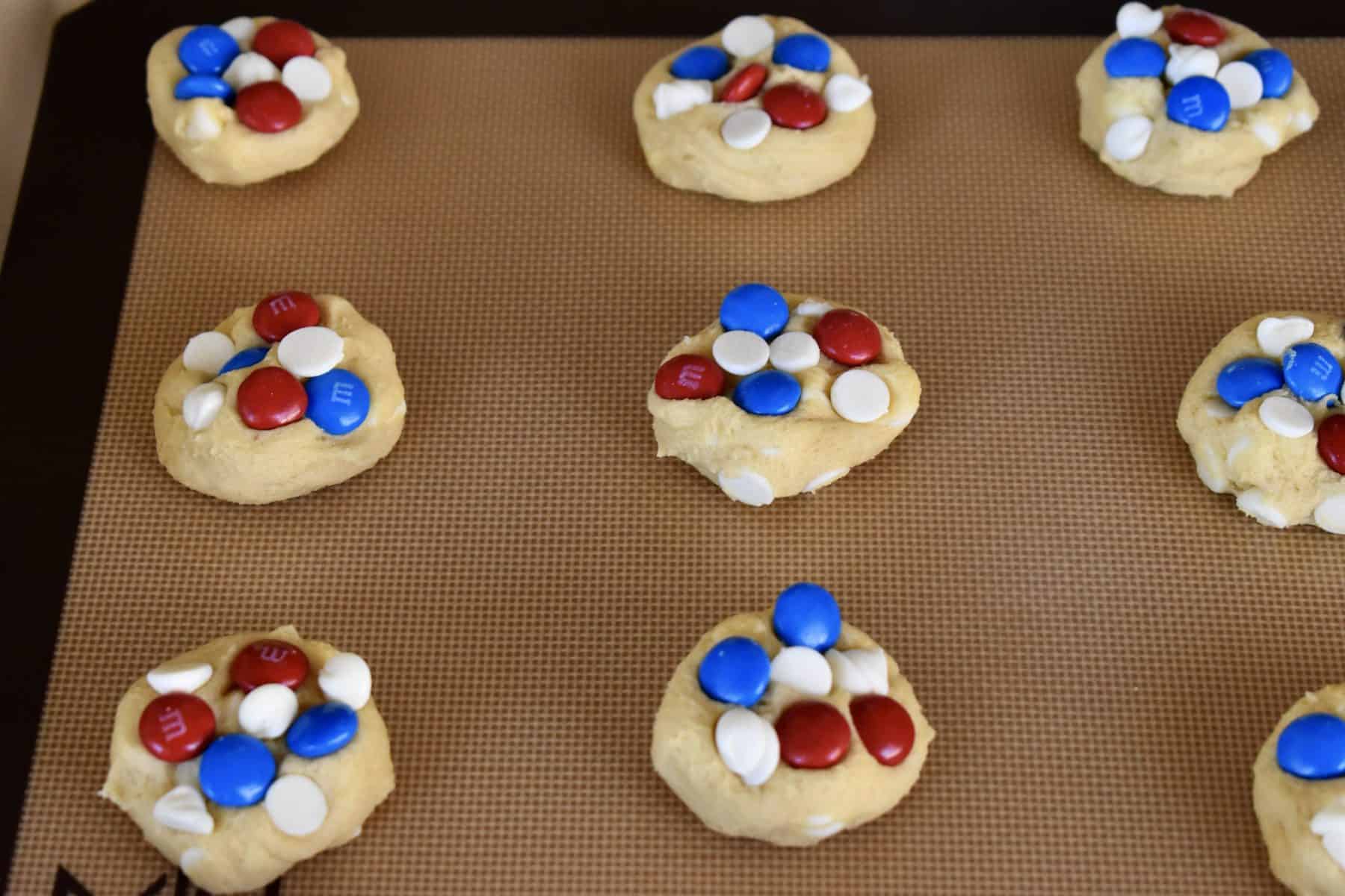 Cookies on a baking sheet with red and blue M&M's pressed into them. 