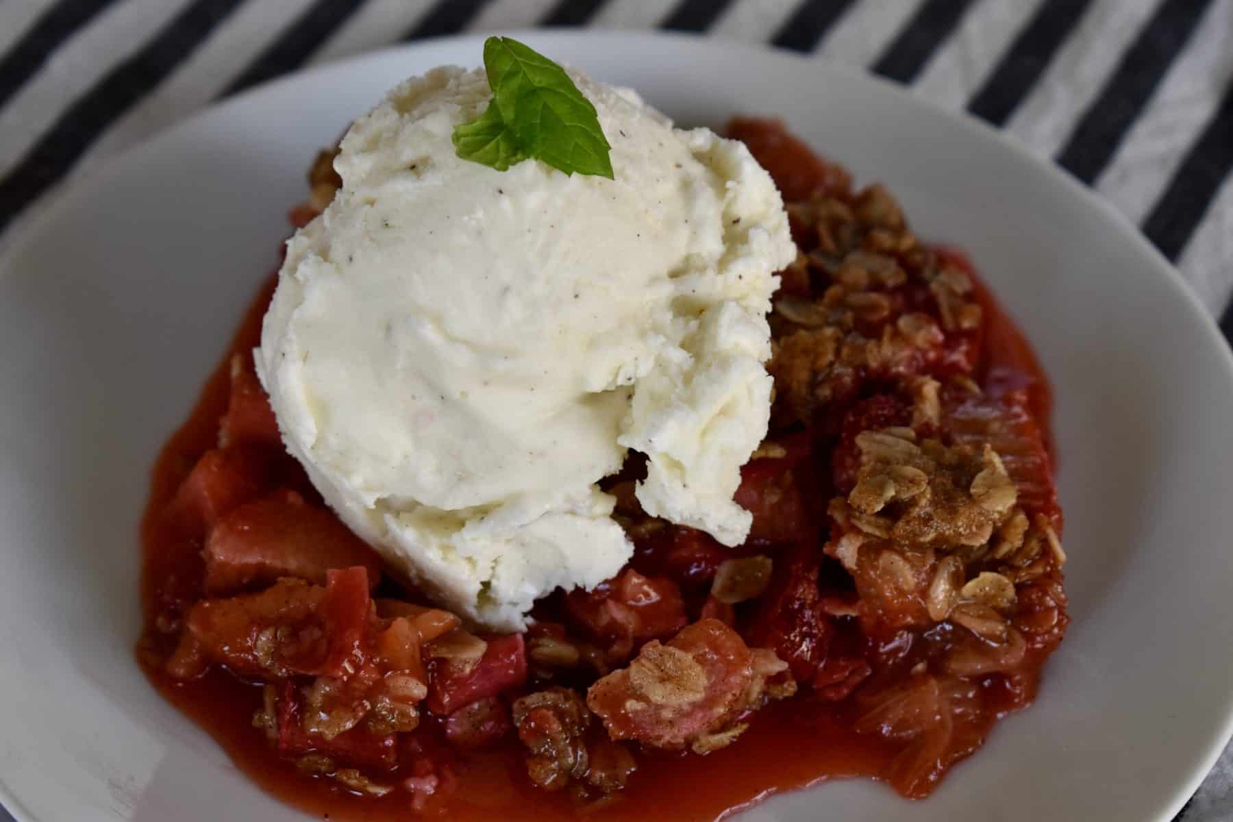 Strawberry Rhubarb Crisp on a white plate with a scoop of vanilla ice cream on top. 