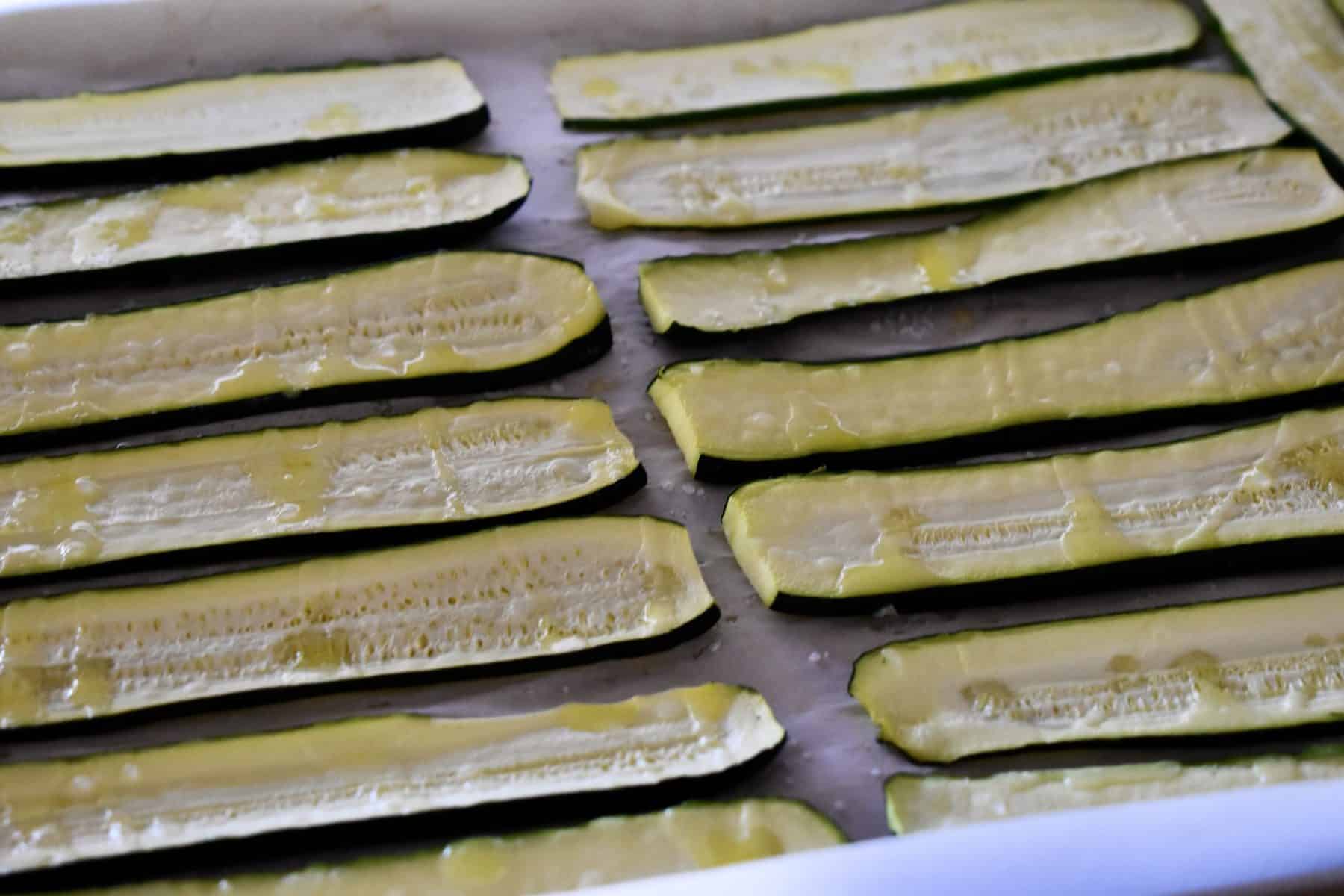 Slices of roasted zucchini on parchment paper in a baking pan. 