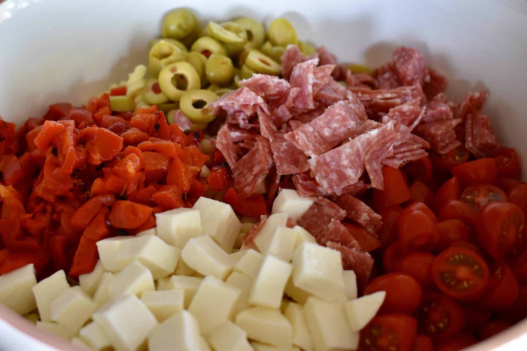 Close up view of the pasta salad with cherry tomatoes, mozzarella, bell peppers, green olives, and salami. 