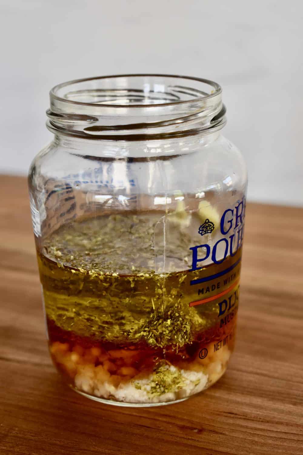 Italian Pasta Salad dressing in a glass jar on a wooden cutting board. 