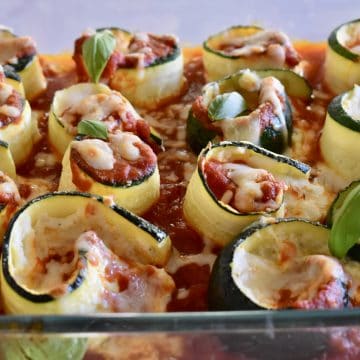Zucchini Ricotta Roll Ups in a glass pan with basil leaves on top.