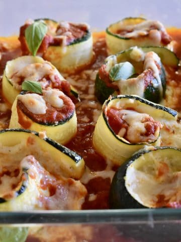 Zucchini Ricotta Roll Ups in a glass pan with basil leaves on top.