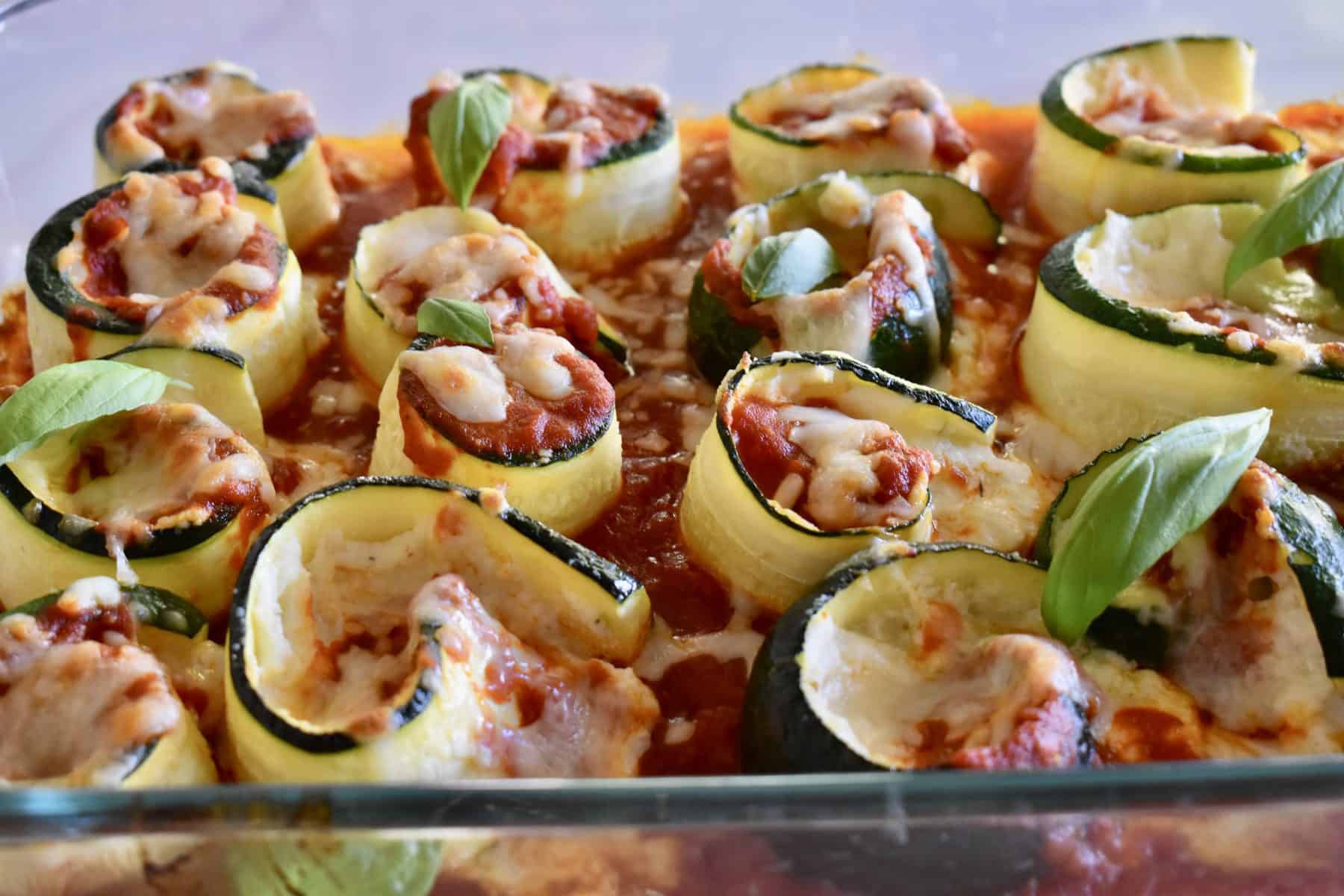 Zucchini Ricotta Roll Ups in a glass pan with basil leaves on top. 