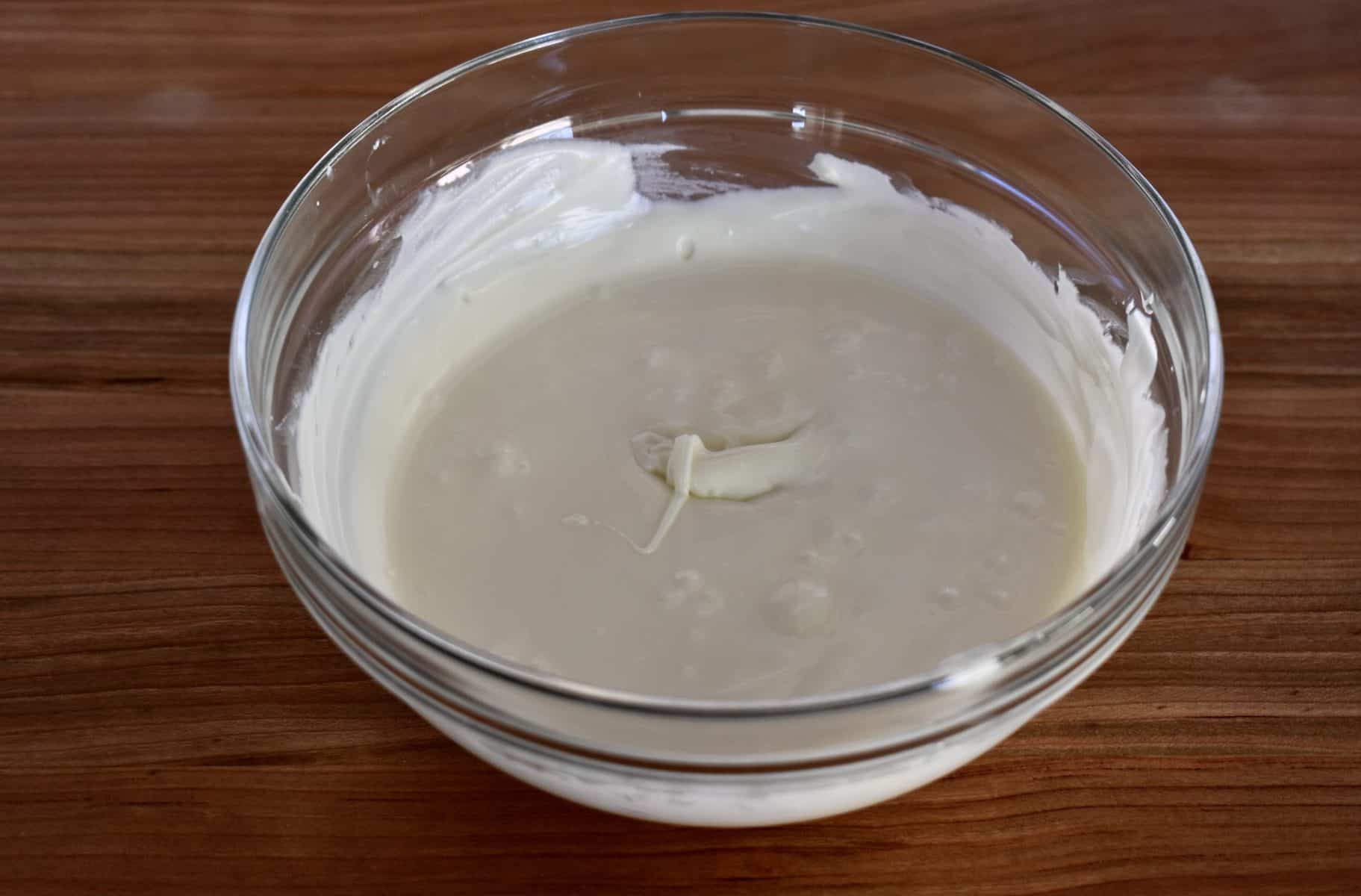 Melted white chocolate in a glass bowl on a wood countertop. 