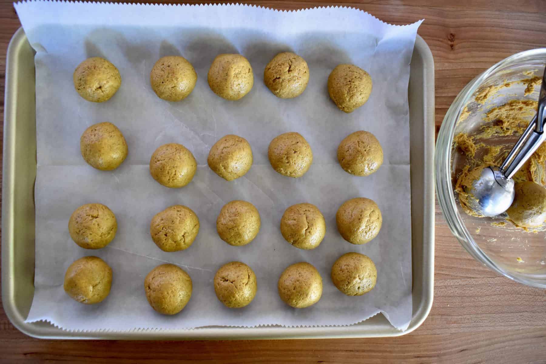 overhead photo of pumpkin spice truffle batter rolled into balls on a lined cookie sheet. 