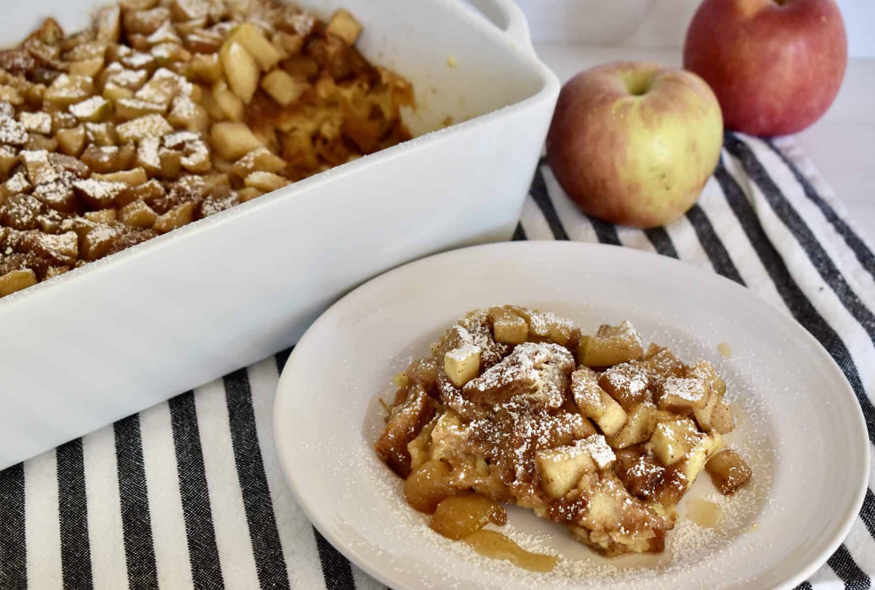 Croissant Baked French Toast in a dish with apples behind it.