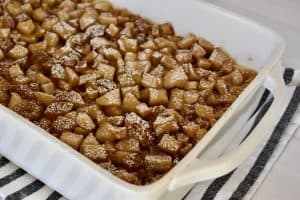 Croissant baked French toast with cinnamon apples in a white baking dish with powdered sugar on top.