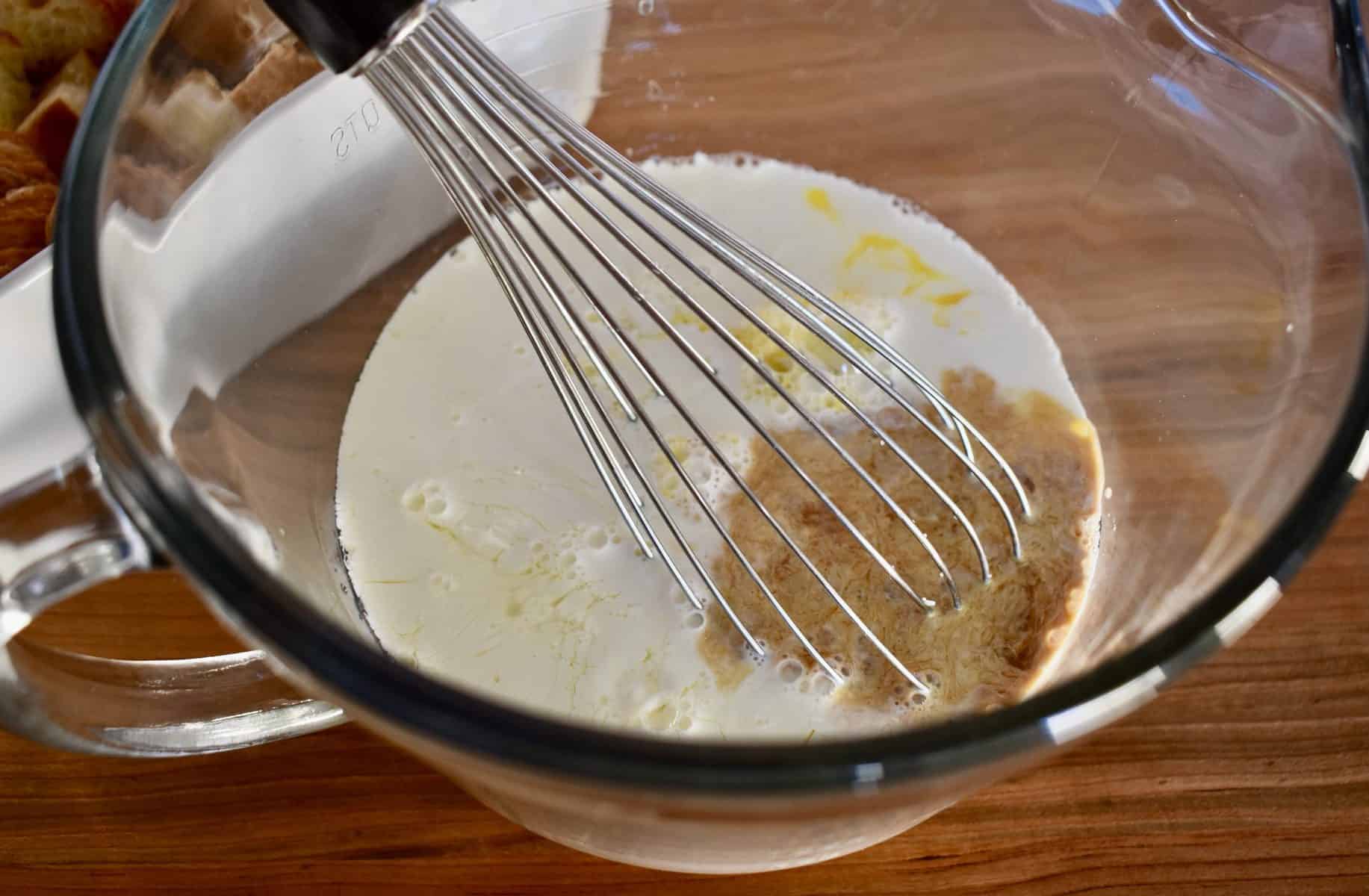 A large glass bowl with half and half, eggs, and vanilla, and a whisk sticking out of it. 