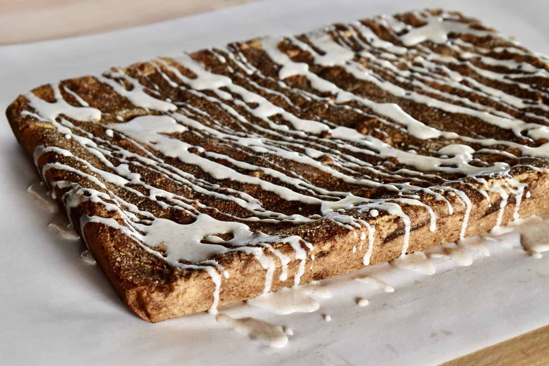 glaze drizzled over the top of the cinnamon sugar blondies on a piece of parchment paper. 
