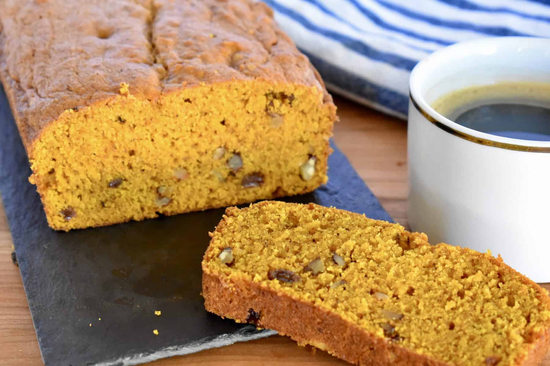 Pumpkin Walnut Raisin Bread on a cutting board with a cup of coffee. 