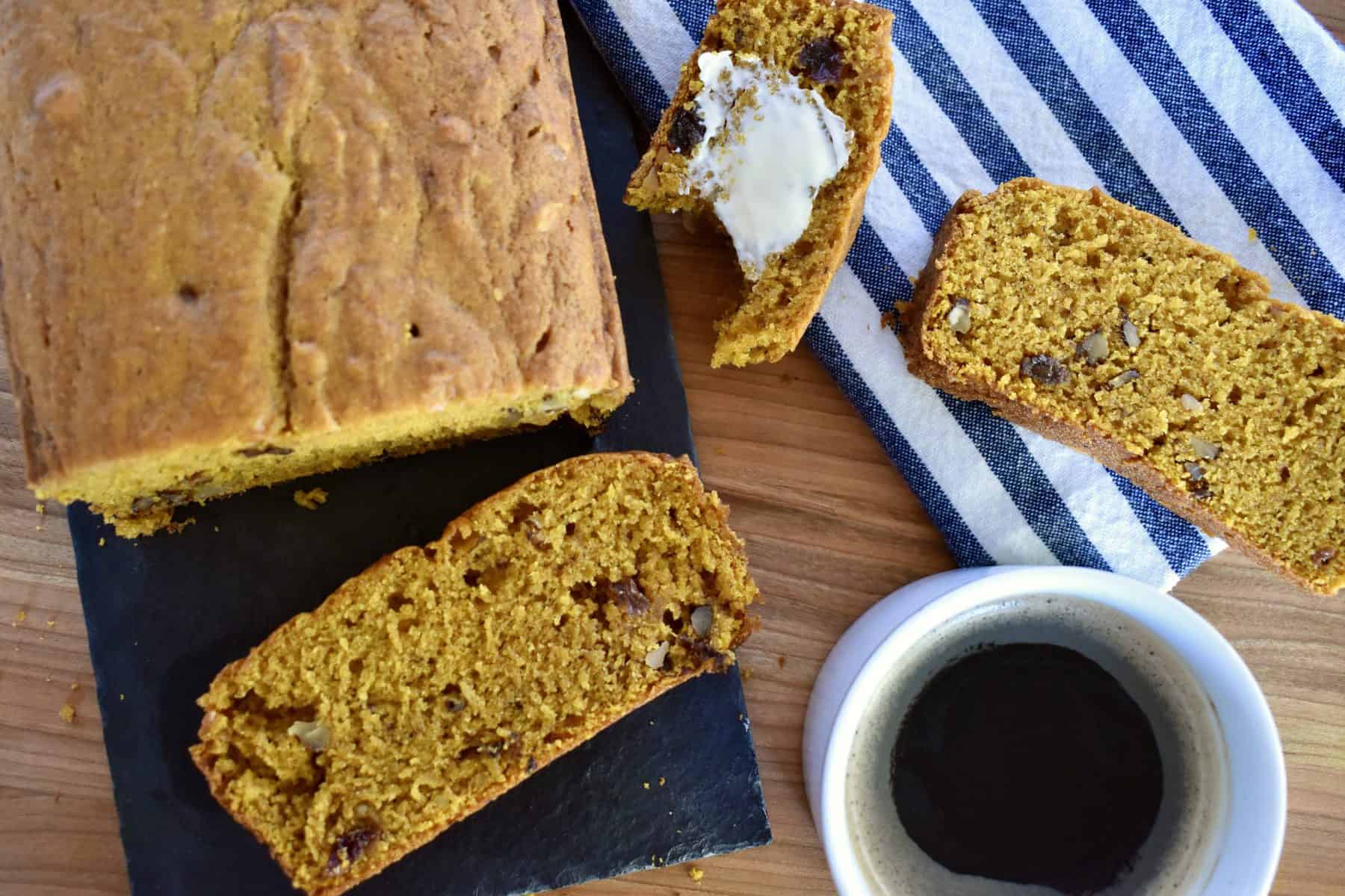 overhead photo of pumpkin bread on a wood cutting board with a cup of coffee. 