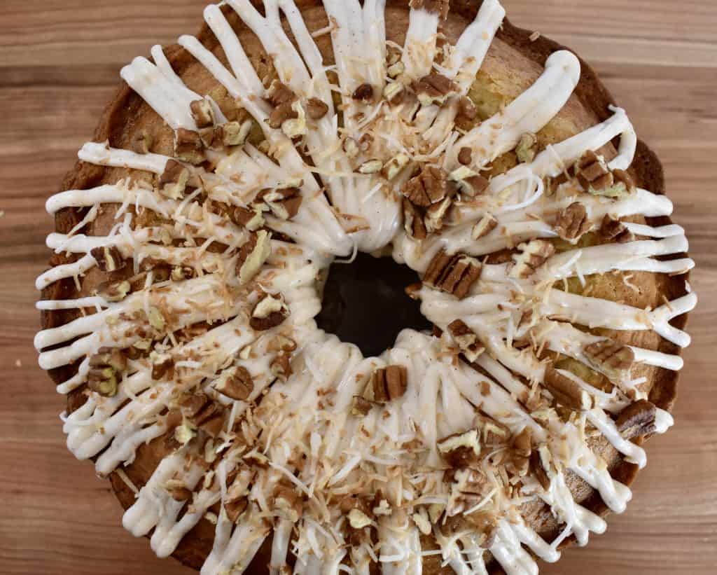 overhead photo of pineapple Bundt Cake with cream cheese frosting and toasted coconut and pecans sprinkled over top. 