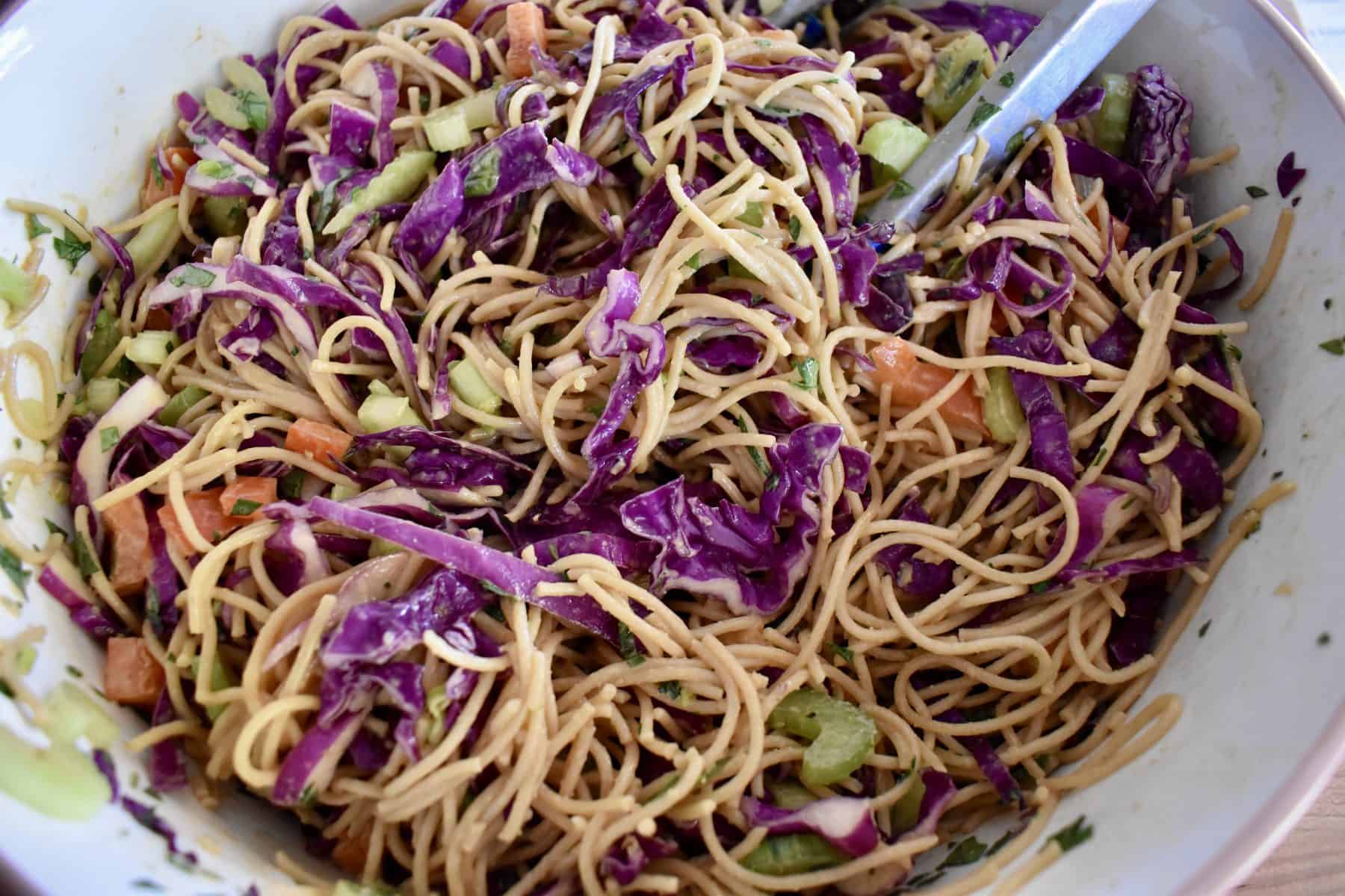 Overhead photo of asian noodle salad in a large bowl with tongs in it. 