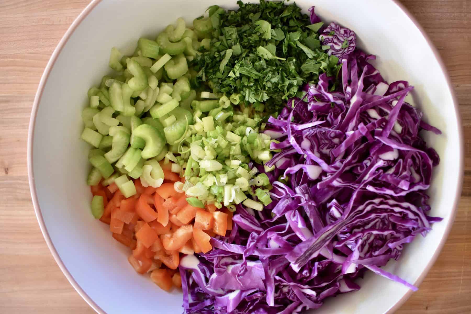 overhead photo of cabbage, celery, bell peppers, green onion, and whole wheat noodles in a large mixing bowl. 