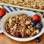 Coconut Pecan Granola in a white bowl with strawberries and blueberries.