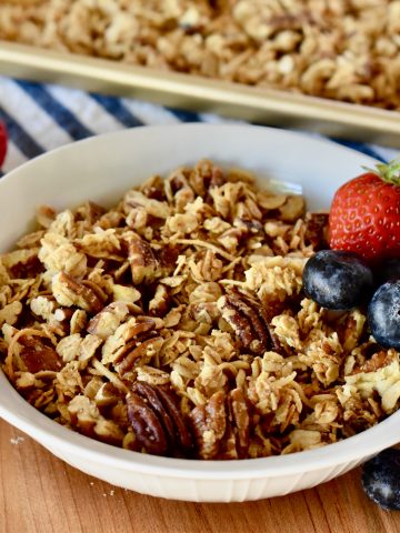 Coconut Pecan Granola in a white bowl with strawberries and blueberries.