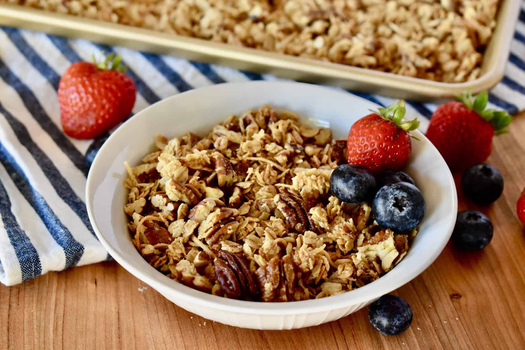 Coconut Pecan Granola in a white bowl with strawberries and blueberries. 