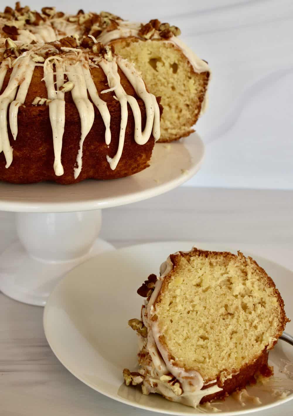 Pineapple Bundt Cake on a white pedestal with slice of cake on plate. 