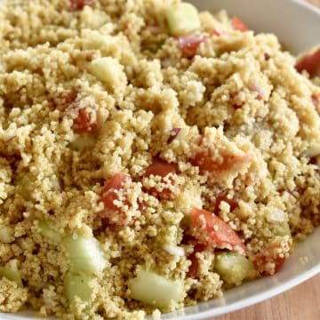 Curried Couscous with tomatoes, cucumbers, and onions in a white bowl.