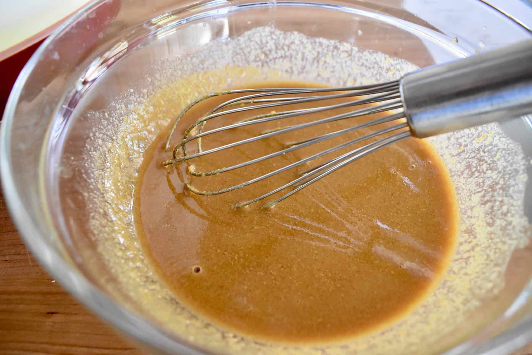 Asian peanut dressing in a glass bowl with a whisk. 