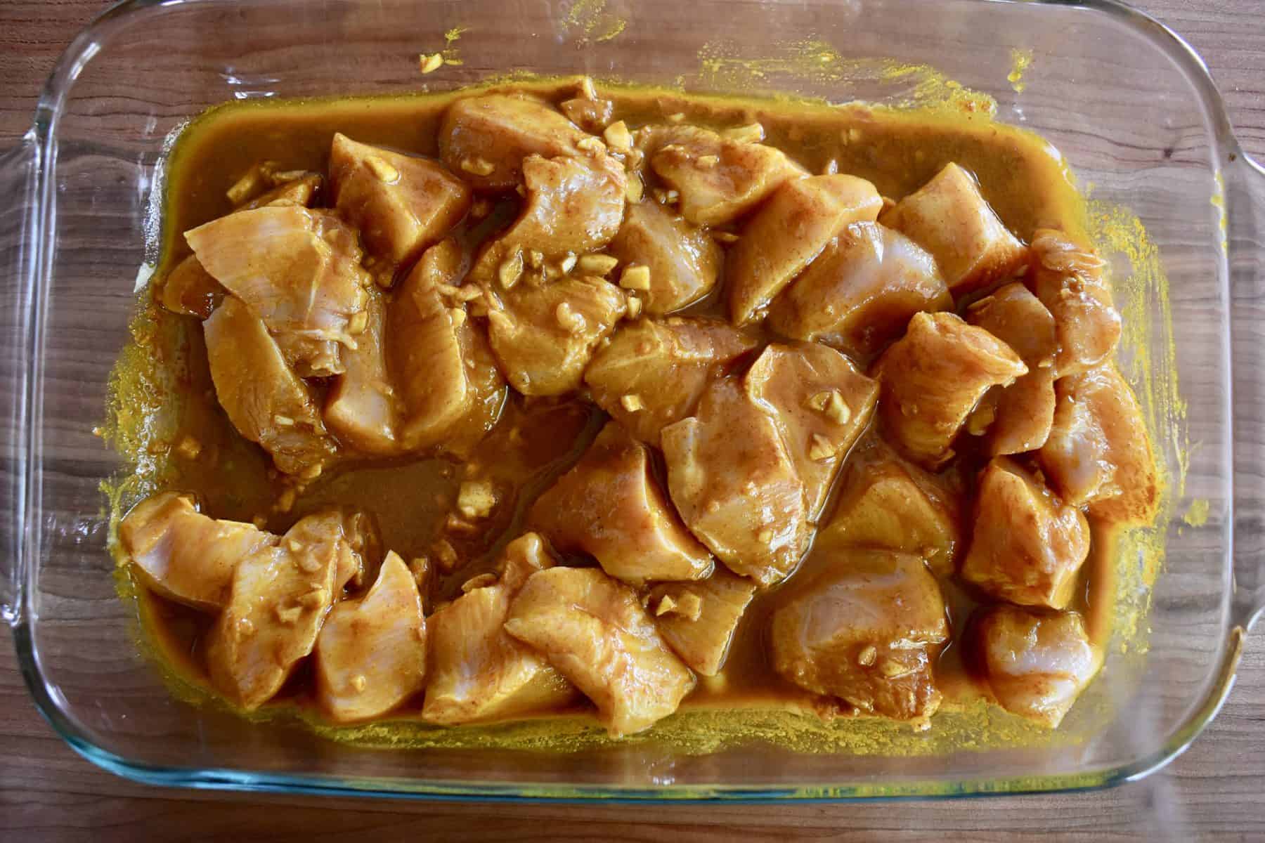 chicken in a glass pan with turmeric marinade poured over top. 