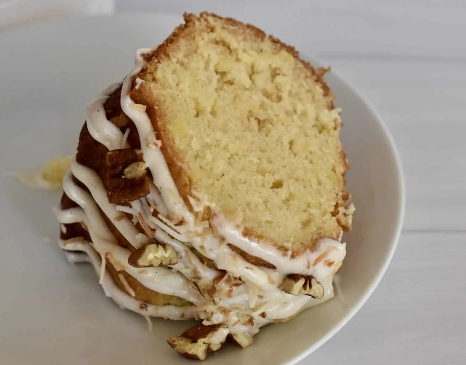 Slice of pineapple Bundt Cake with cream cheese frosting on a white plate. 