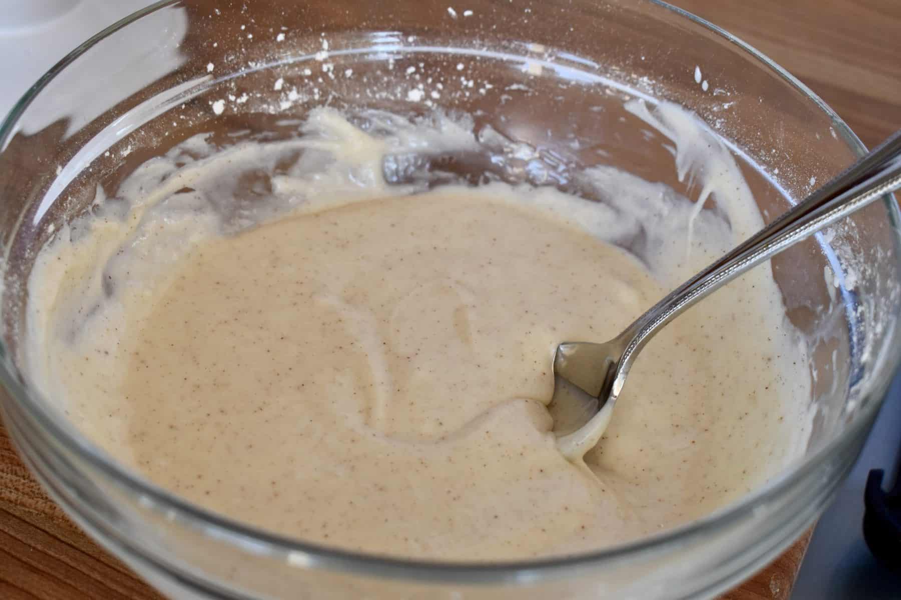cinnamon cream cheese frosting in a glass bowl with a spoon. 