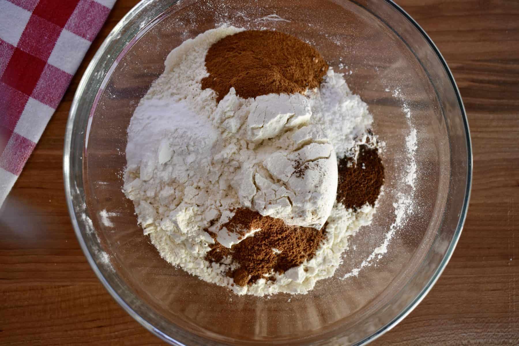 overhead photo of flour, baking powder, salt, and spices in a bowl with a whisk. 