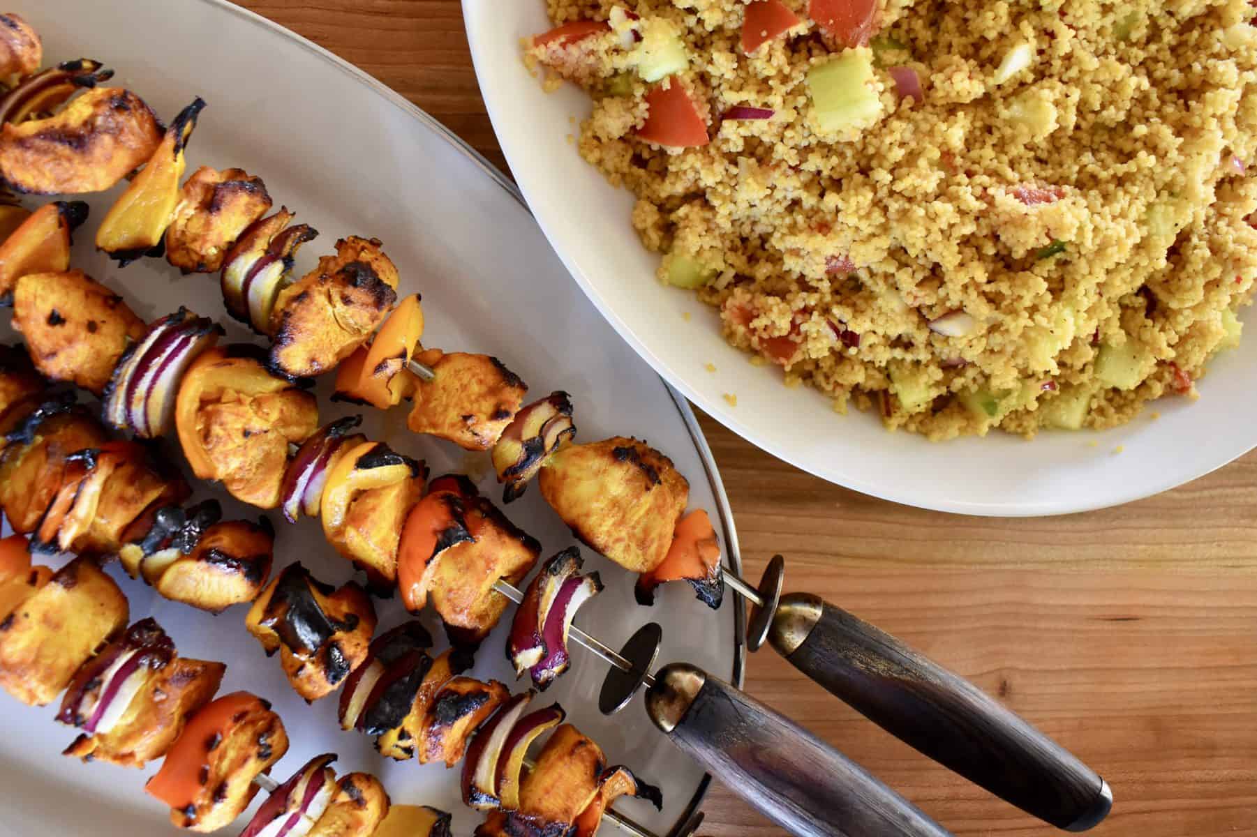 overhead photo of grilled chicken kabobs on a plate with couscous. 