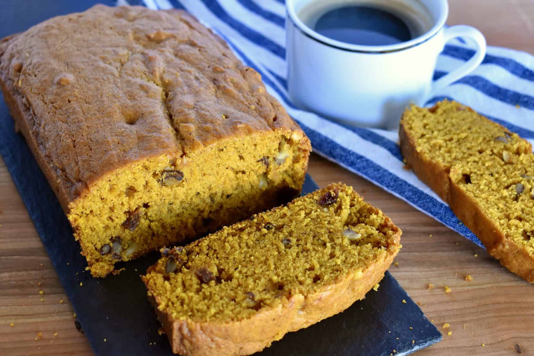 Pumpkin Walnut Raisin Bread on a cutting board with a cup of coffee. 